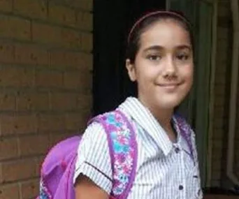 A young girl smiling, wearing a striped school uniform and a purple floral backpack.