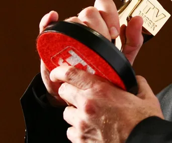 Two hands holding a gold TV Week Logie Award with a red-patterned circular base.