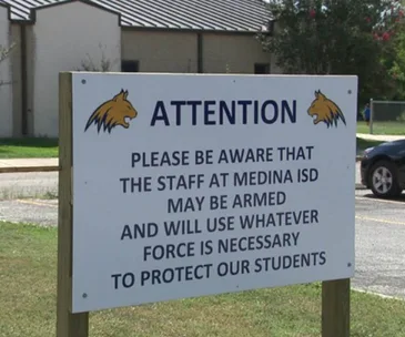Sign at Medina ISD warns staff may be armed to protect students, featuring a bobcat logo.