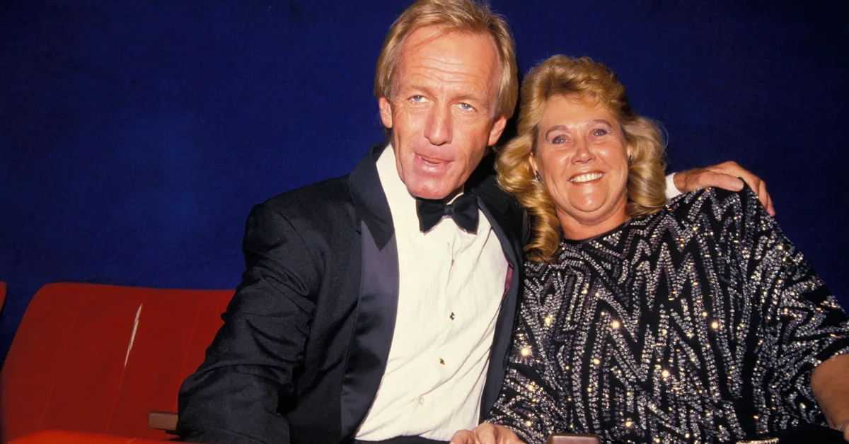 A man in a tuxedo and a woman in a sparkly dress sit together, smiling at the camera.