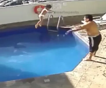 Man pushes child into a blue pool, captured on CCTV, near a ladder and lifebuoy on the wall.