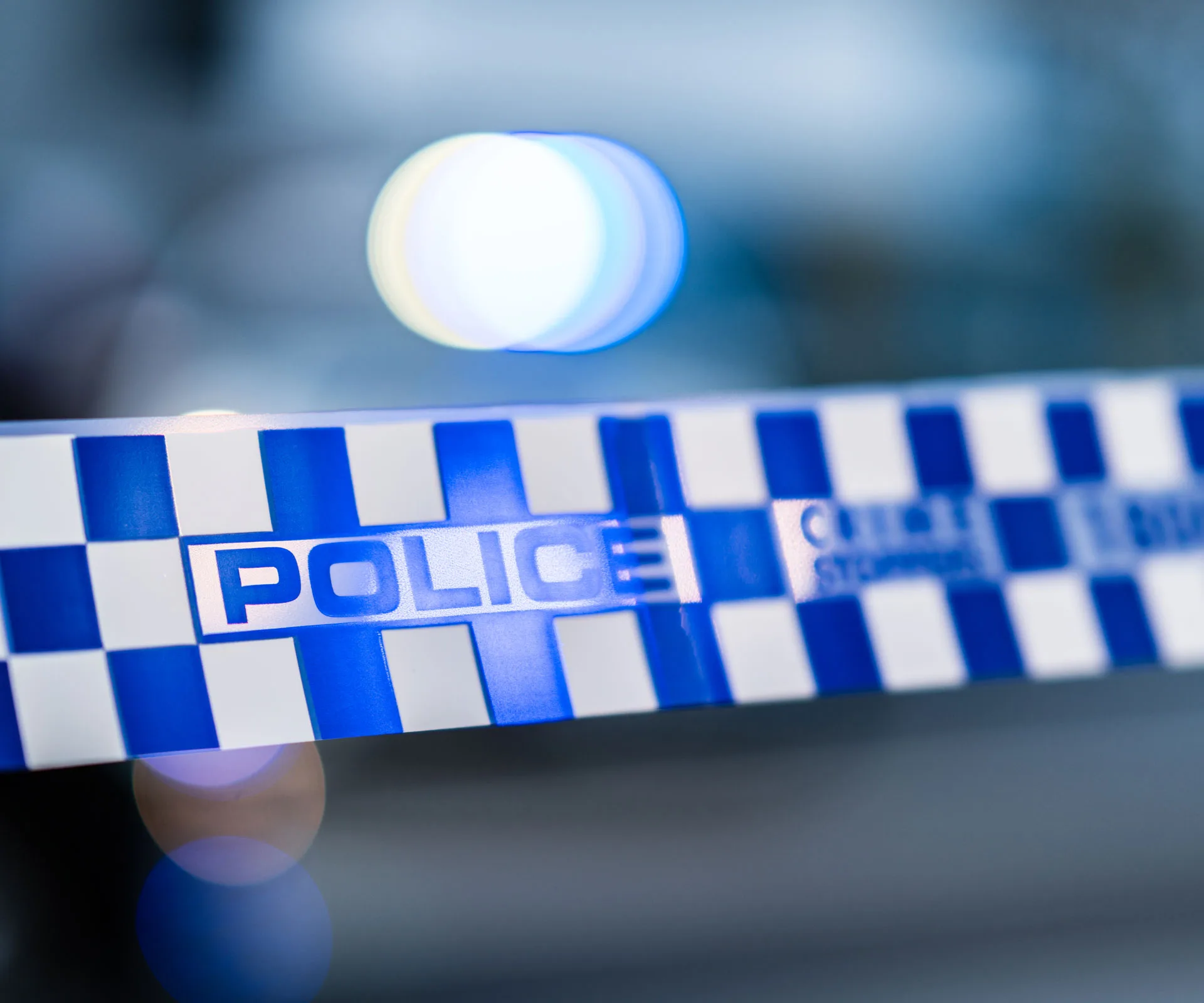 Close-up of blue and white police tape with blurred lights in the background.