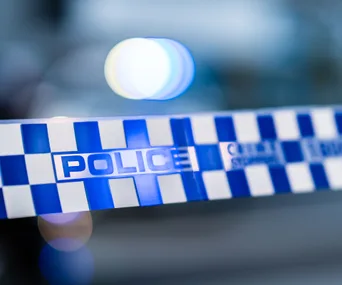 Close-up of blue and white police tape with blurred lights in the background.
