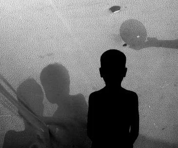 Silhouette of a child against a textured background with shadows of figures interacting.