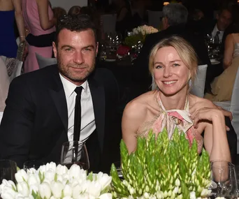 Man and woman smiling at a formal event, seated at a table with flowers and wine glasses.