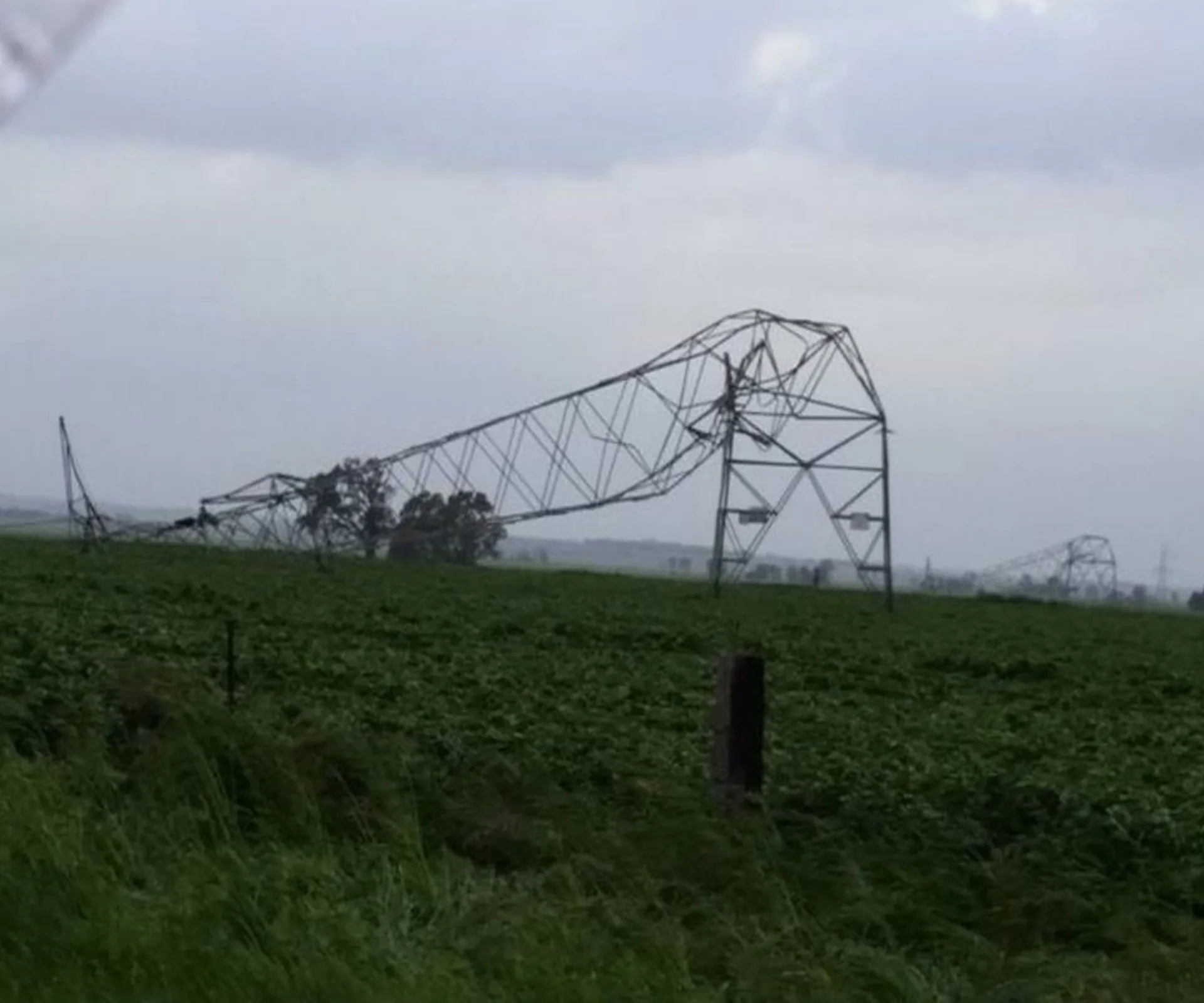 Bent transmission tower in a field after wild storms in South Australia under a cloudy sky.