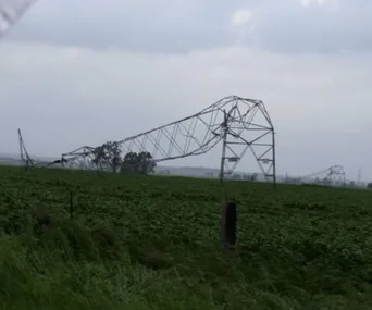 Bent transmission tower in a field after wild storms in South Australia under a cloudy sky.