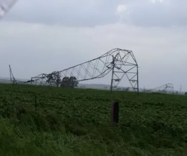 Bent transmission tower in a field after wild storms in South Australia under a cloudy sky.