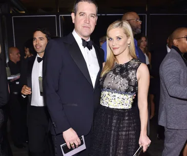 A couple dressed formally at an event, with others around them in the background.