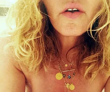 Blonde individual wearing necklaces with gold pendants and jeweled grillz, partially visible face.