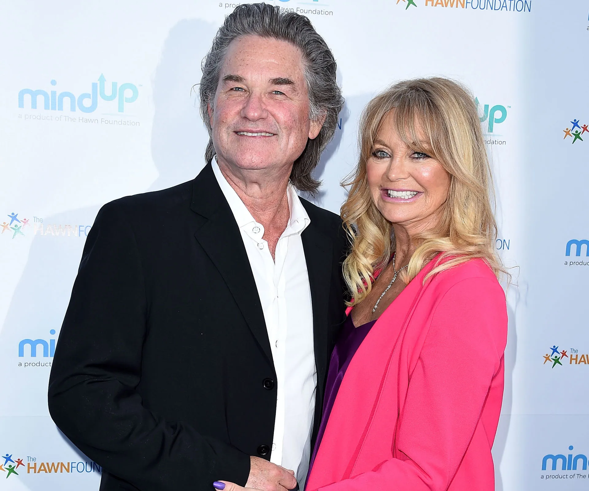 Goldie Hawn and Kurt Russell smiling at a red carpet event, in front of a backdrop with "Mind Up" and "Hawn Foundation" logos.