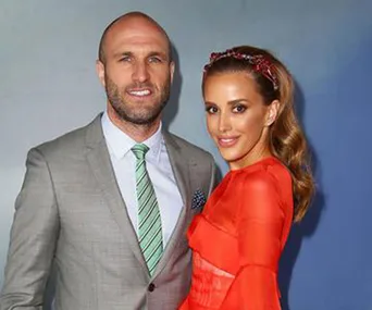 Man in a gray suit with a green tie and woman in a red dress with wavy hair and a headband, posing together.