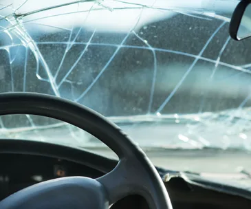 Cracked windshield view from inside a car with visible steering wheel.