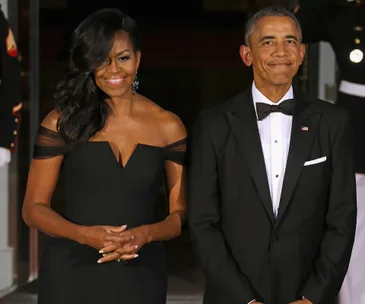 Barack and Michelle Obama standing together in formal attire, smiling at an event.