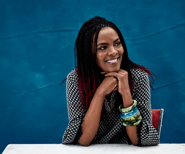 Smiling woman with braided hair and colorful bangles, posing against a blue background.
