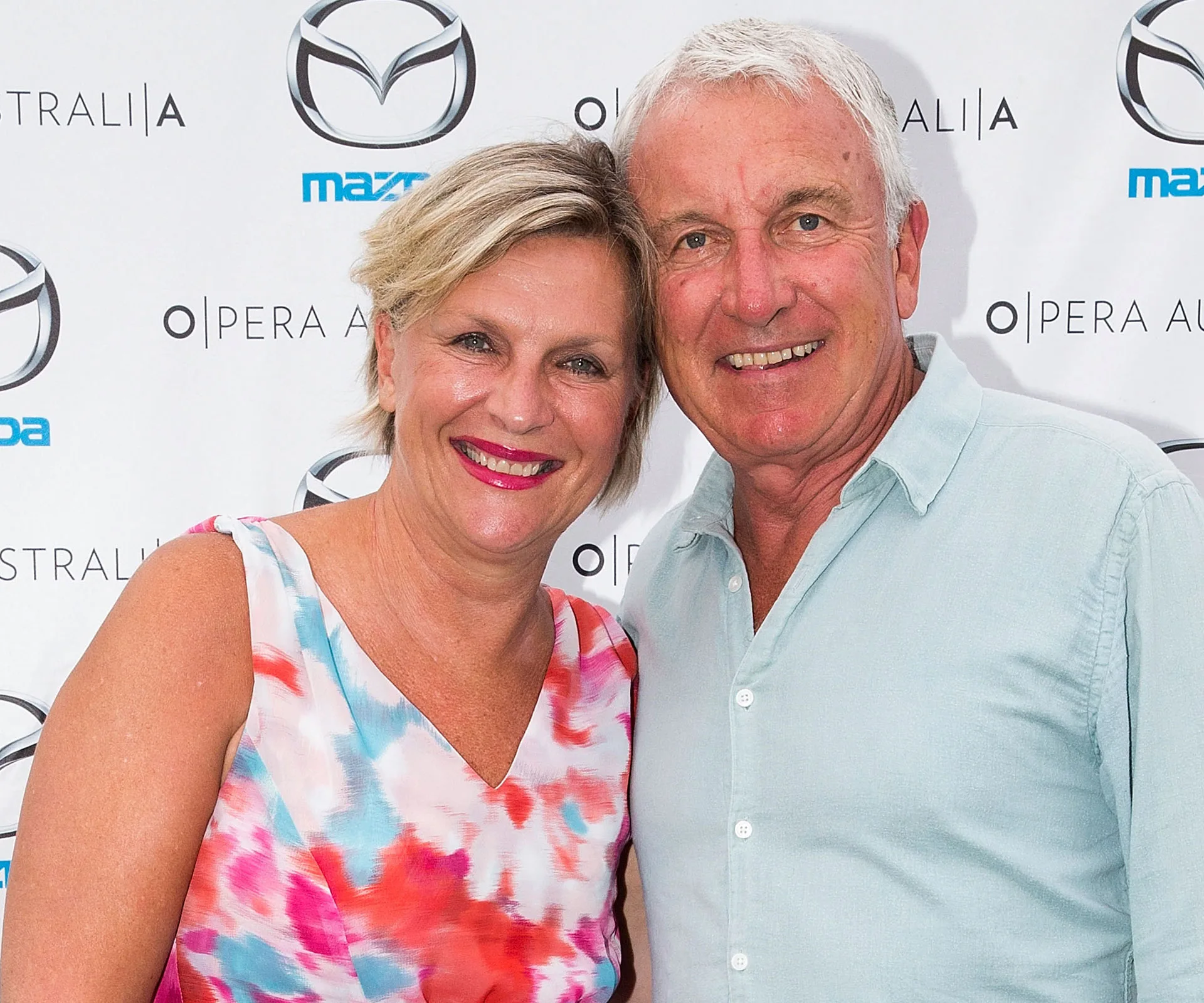 A smiling woman in a colorful dress and a man in a light shirt pose together in front of a branded backdrop.