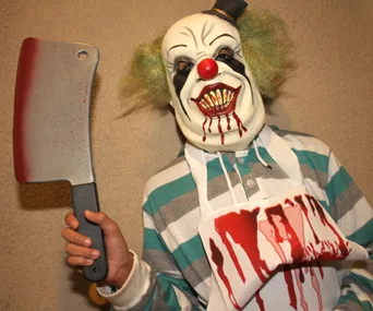 A person in a creepy clown mask with a fake cleaver and a bloody apron, associated with the creepy clown craze.