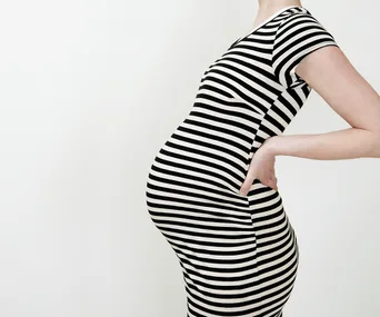 A pregnant person in a black and white striped dress, side view with hand on hip.
