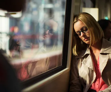 Person sleeping on a train, leaning against the window, bathed in soft light.