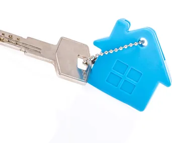 Steel key with blue house-shaped keychain on white background, symbolizing home ownership.