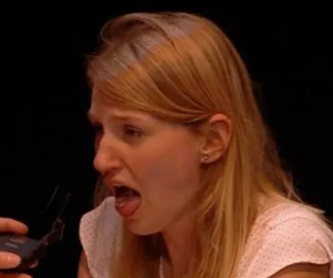 A woman with a surprised expression opens her mouth while a man holds glasses near her face.