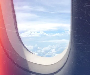 View of clouds and sky through an airplane window, with sunlight casting a glow on the frame.