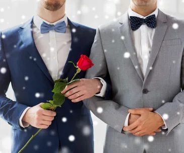 Two men in suits, one with a red rose, standing arm in arm, with a soft, blurred effect resembling snowfall.