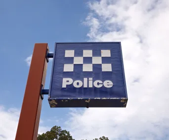 Police sign against a blue sky background, featuring a blue and white checkered pattern and the word "Police" in white.