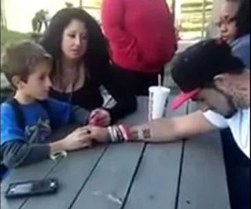Father tells young son about mother's death from drugs at a picnic table, with supportive adults nearby.
