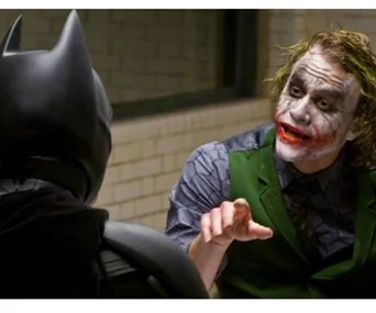 Batman facing the Joker in dimly lit room, Joker gesturing animatedly.