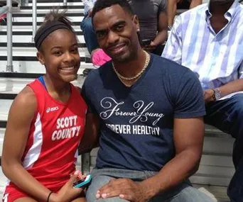 Father and daughter sitting together, smiling at an outdoor sports event.