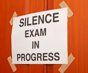 Sign on a door reads, "Silence Exam in Progress," taped at four corners.