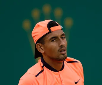 Tennis player in an orange outfit and cap facing forward, green background with blurred logo.