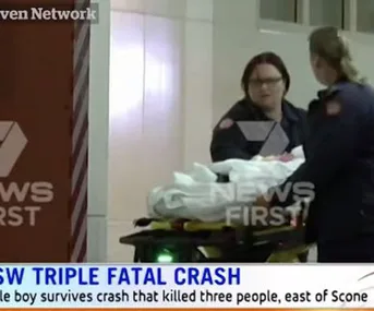 Paramedics moving a stretcher covered with a white sheet; overlaid text reports on a triple fatal crash in NSW.