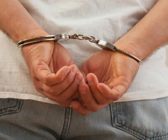 Hands in handcuffs behind back, wearing jeans and white shirt.