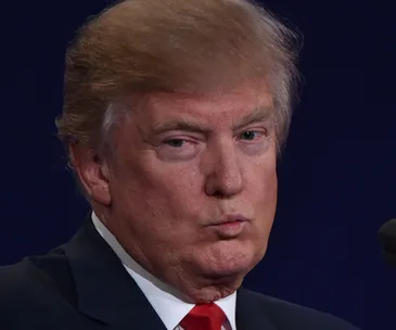 A person with blond hair and a suit is making a face during a debate.
