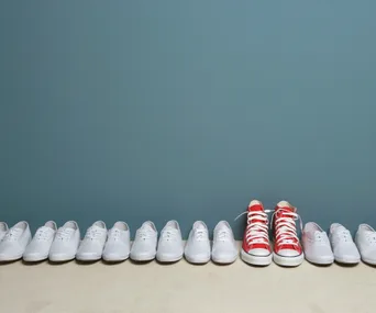 Row of white sneakers with a standout pair of red sneakers in the middle against a blue background.