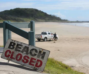 Beach closed sign with a truck and person on a deserted Byron Bay beach, amidst a shark safety alert.