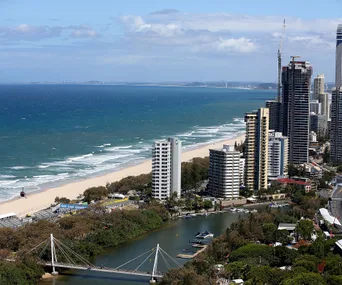 Aerial view of Gold Coast, Australia, featuring skyscrapers, a beach, and a river with a bridge in the foreground.