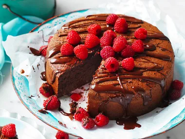 Chocolate cake with raspberries and chocolate drizzle on a floral plate, one slice removed.