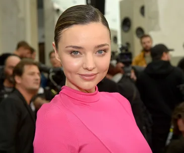 Alt text: "Person in pink top at an event, with people and cameras in the background."