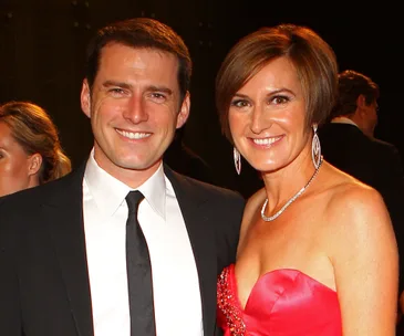 A man in a black suit and tie smiles alongside a woman in a red dress at an event.