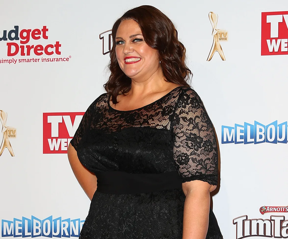 A person smiling in a black lace dress at a TV Week event, with logo banners in the background.