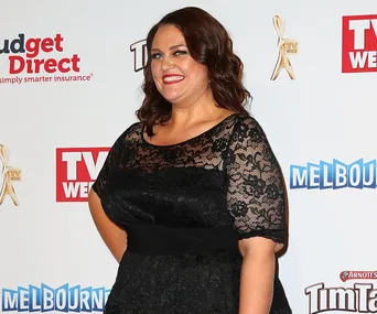 A person smiling in a black lace dress at a TV Week event, with logo banners in the background.