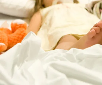 A child in a hospital bed with a stuffed orange fox beside them.