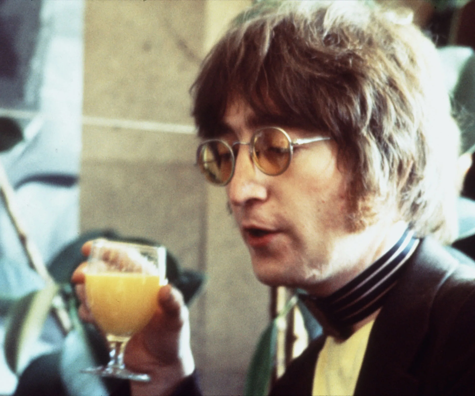A man with glasses holding a glass of orange juice.