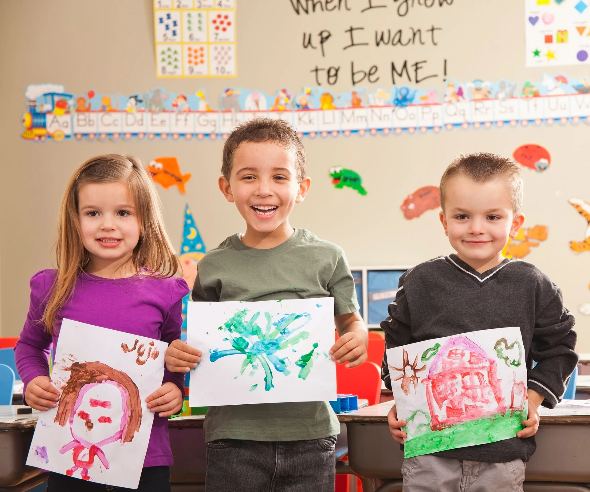 Children in a classroom proudly holding up their colorful paintings.