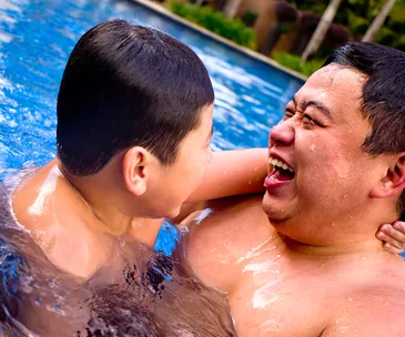 Father and child joyfully playing in a swimming pool, laughing and embracing each other.