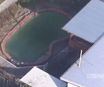 Aerial view of a backyard with a fenced, kidney-shaped swimming pool near a building.