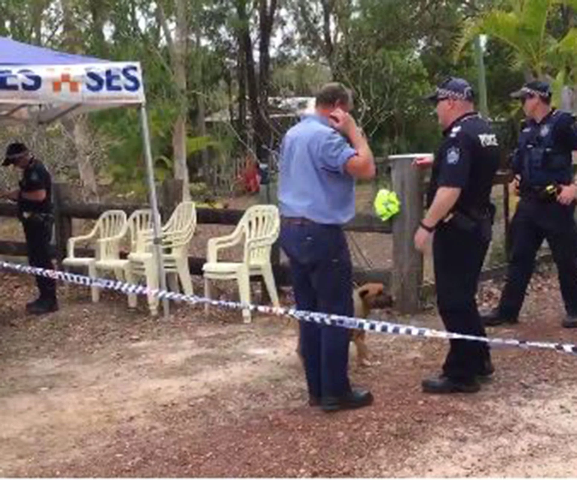 Police and emergency services at rural scene with chairs and taped off area.